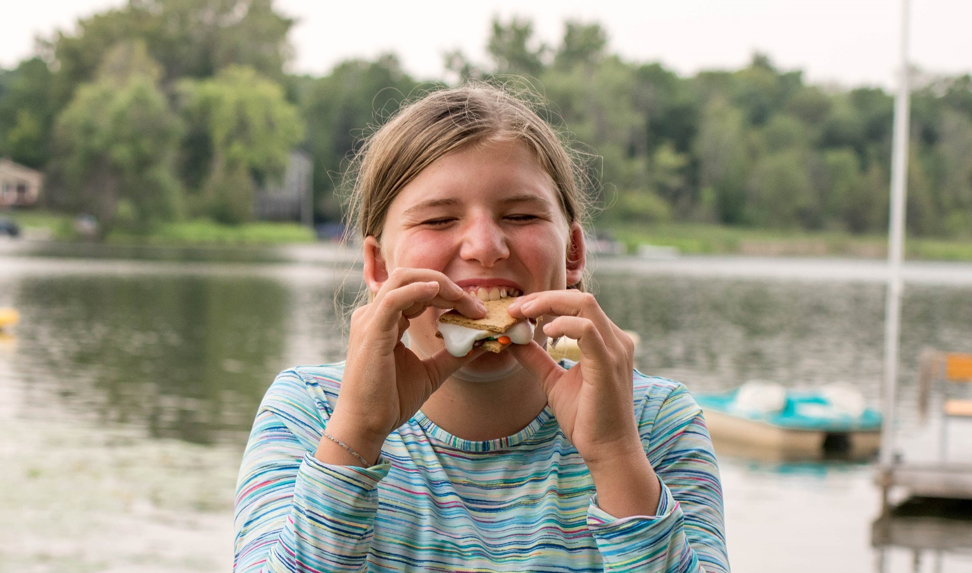 A girl takes a bite out of a smore. Campfire recipes shared by Pear & Simple, a gift boutique in Port Washington, WI.